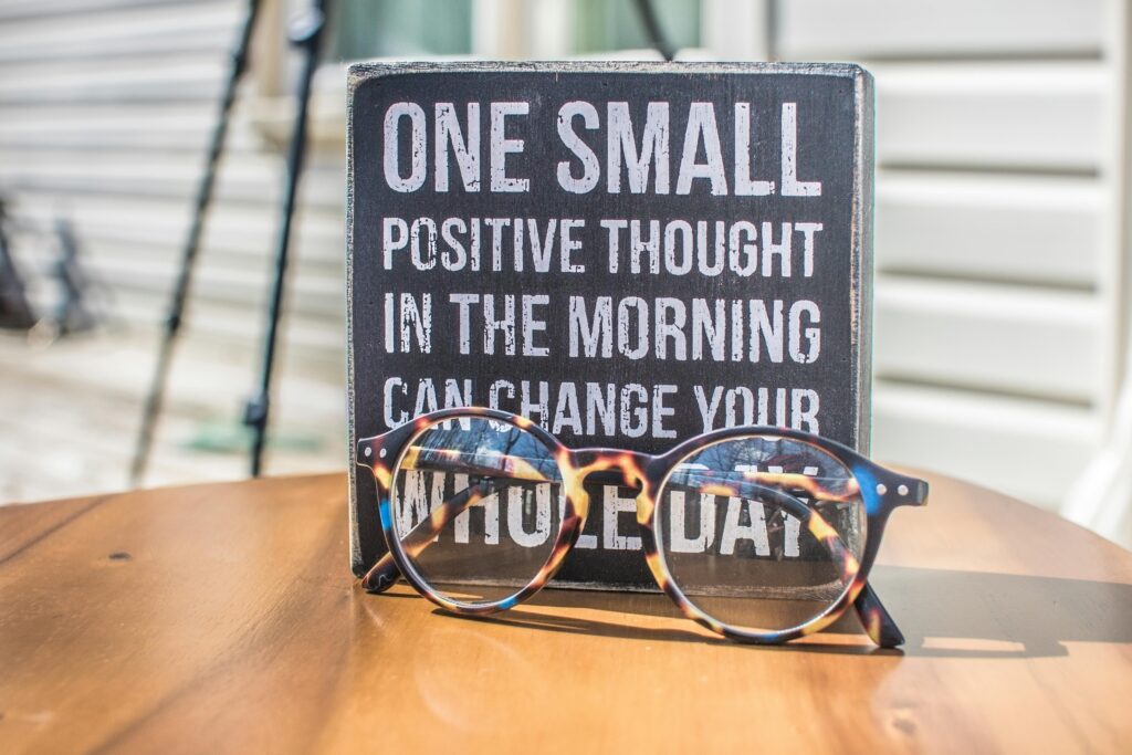 Eyeglasses resting on a table in front of a motivational quote sign emphasizing positivity