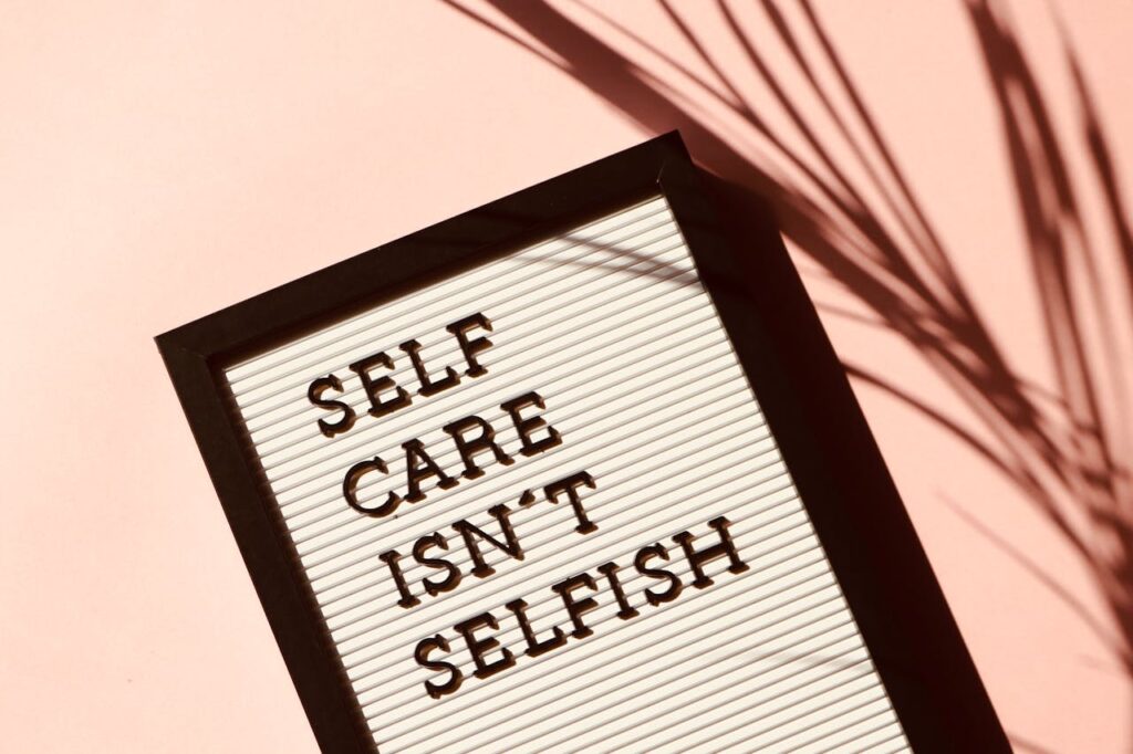 Letter board displaying Self Care Isnt Selfish with artistic shadow on pink background