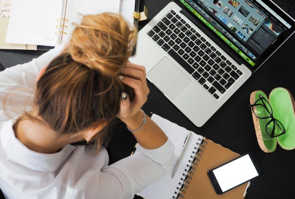 Overhead view of a stressed woman working at a desk with a laptop phone and notebooks