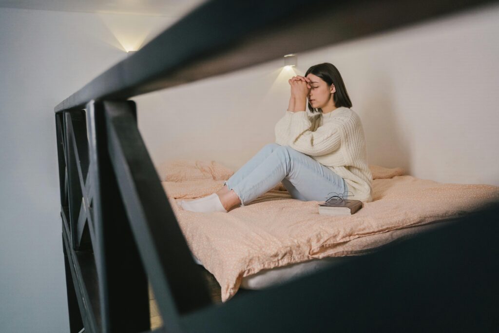 Woman in a cozy knitted sweater meditates peacefully on the bed with closed eyes and praying hands.